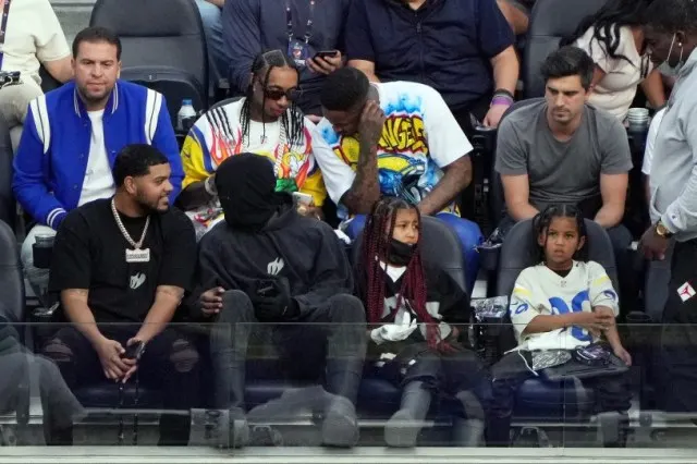 Kanye West -- all in black and wearing his now-standard mask -- takes the game with his kids North and Saint along with another KarJenner-adjacent rapper ex, Tyga (in sunglasses).