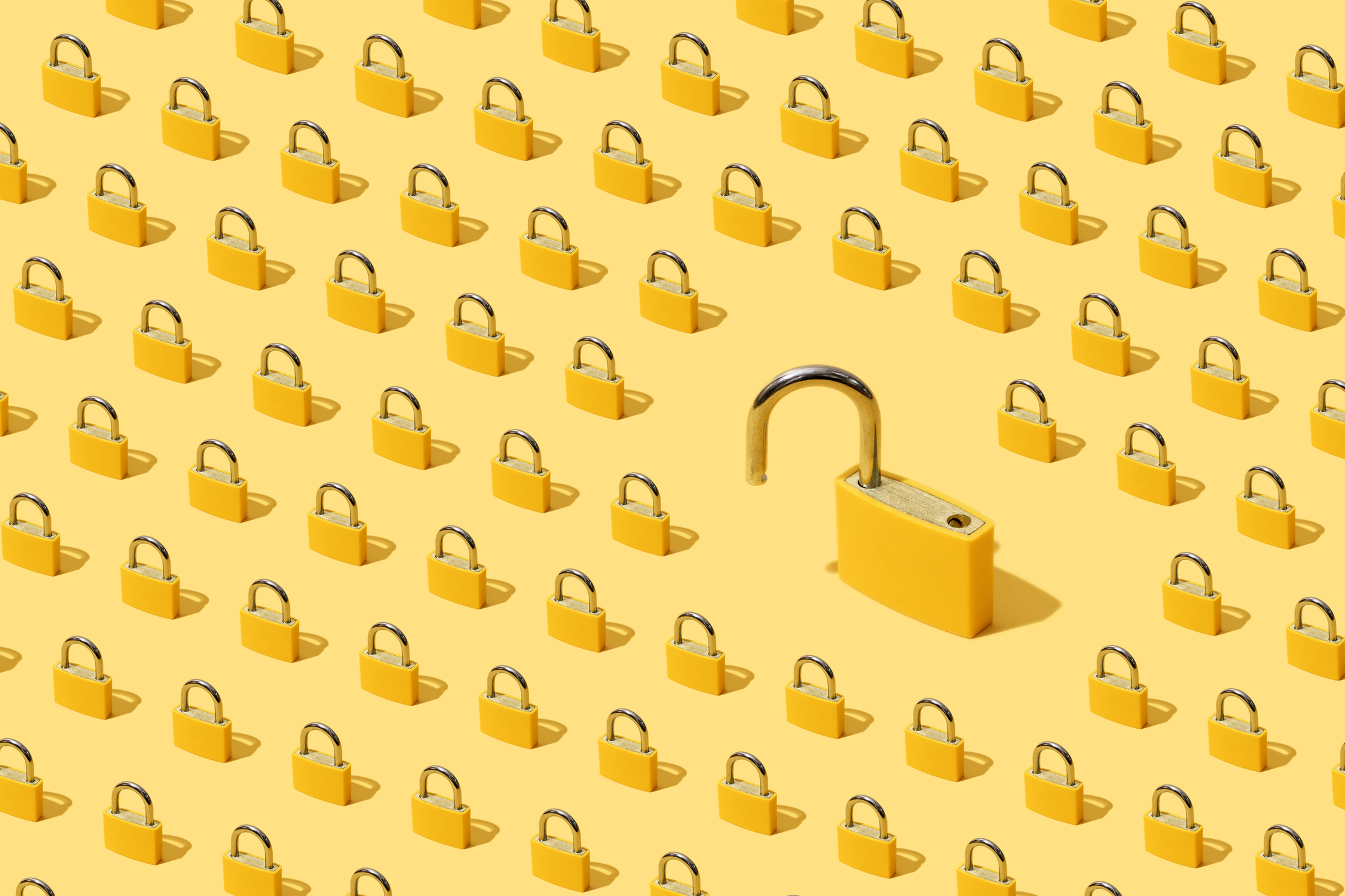 High angle view of many yellow padlocks on yellow background. One of them is open.